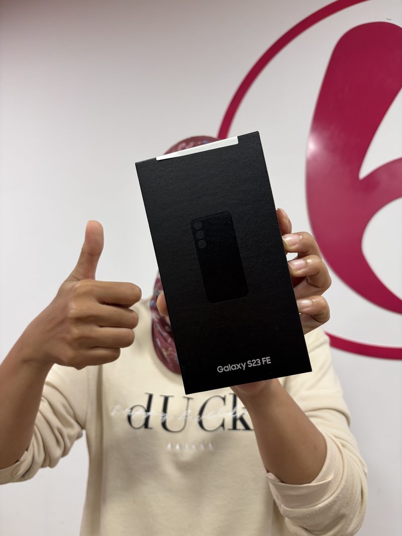 Happy Berry Nice customer holding a Samsung Galaxy S23 FE box in front of the brand wall after a sale